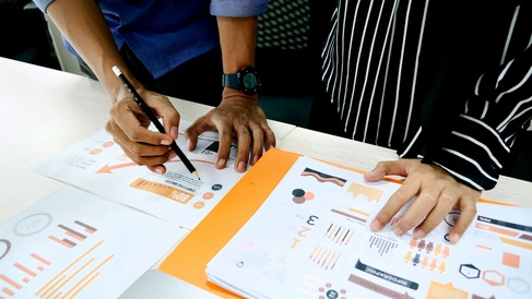 Two people discussing some printed documents spread out on a desk.