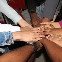 View from above. Half a dozen hands of differing races and skin colours, placed on top of one another in a circle.